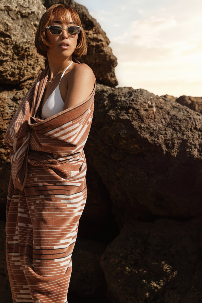MORELIA ORGANIC BEACH TOWEL | Woman wrapped in a brown towel against rocks